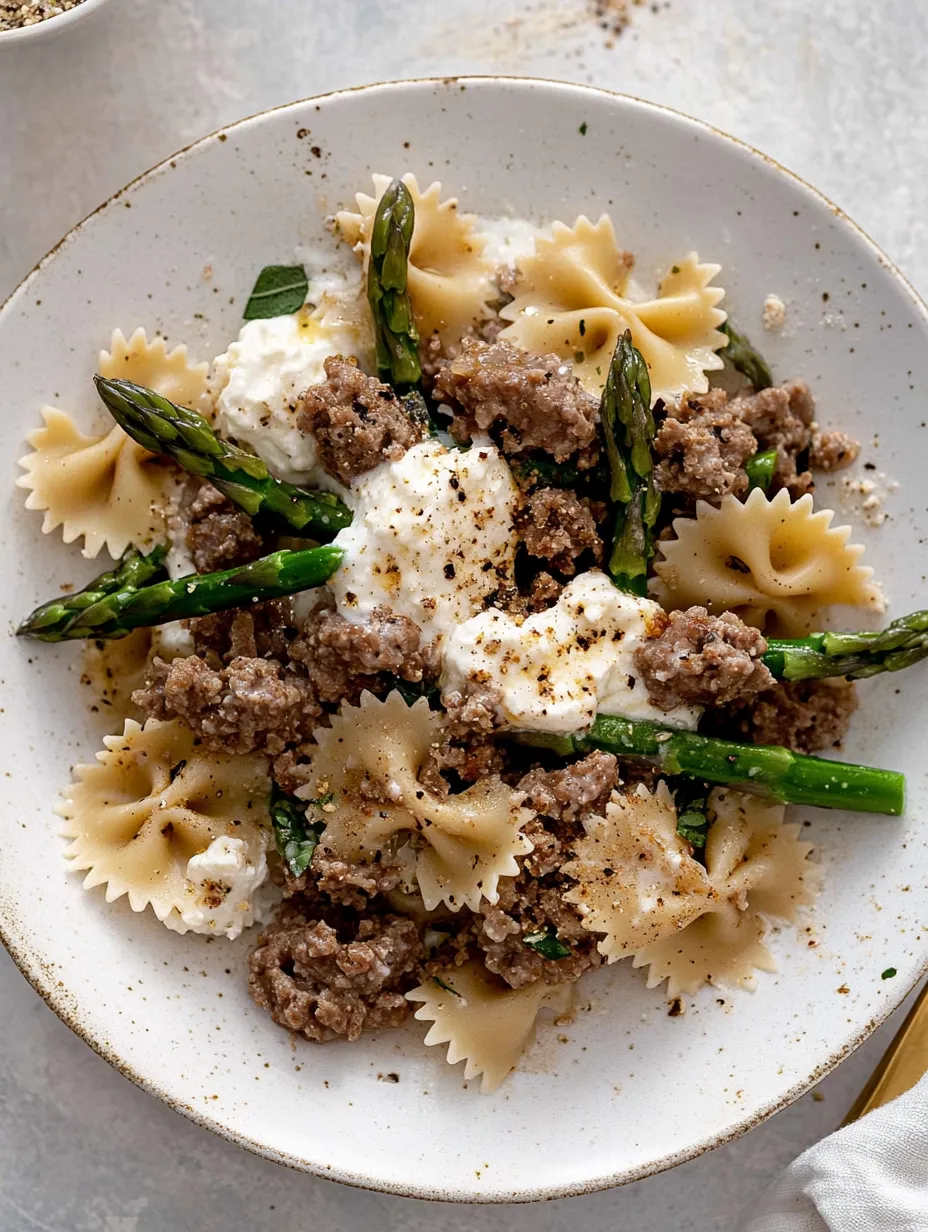 Ein Teller mit Pasta, Wurst und Spargel.