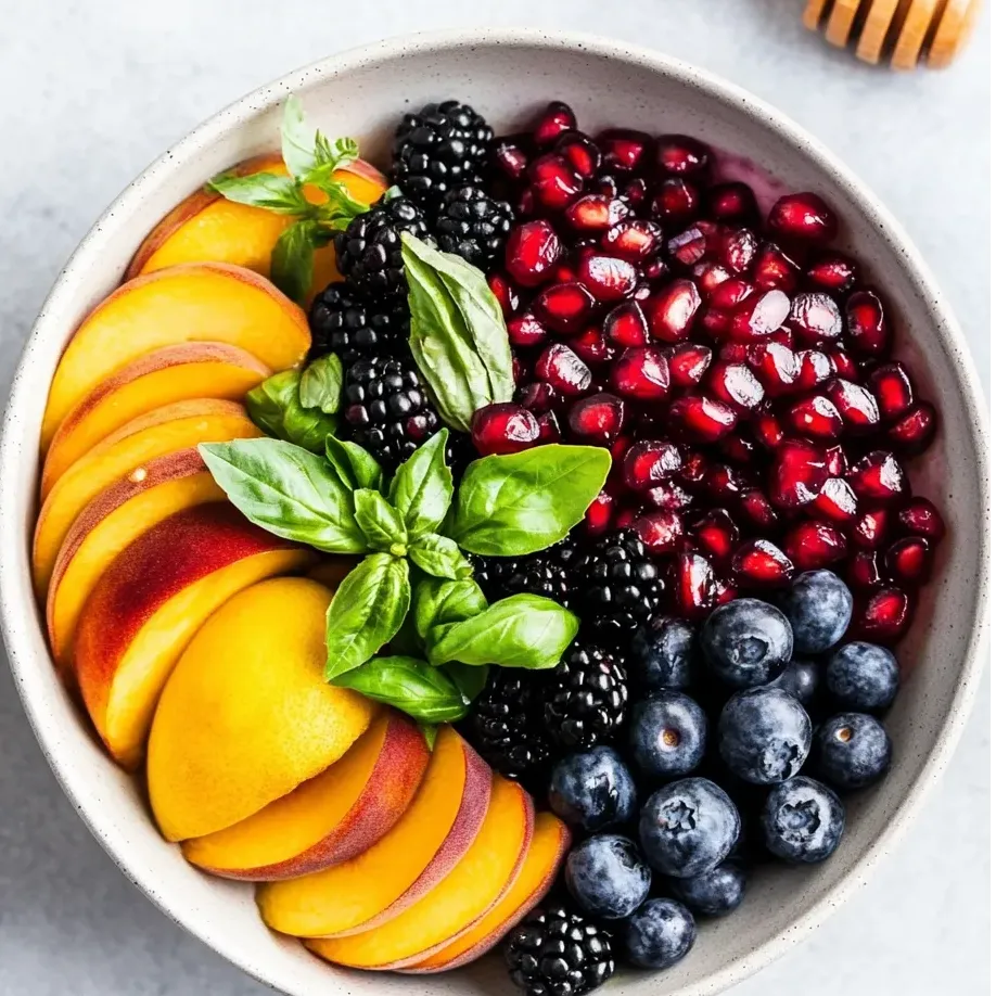 Schüssel mit Obst: Heidelbeeren, Brombeeren, Pfirsichen und Honig.