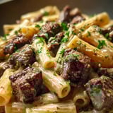 Eine Portion Pasta mit Steakstücken und frischen Kräutern.