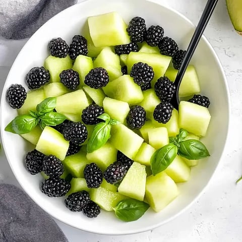 Eine Schüssel Fruchtsalat mit Brombeeren, Honigmelone und Basilikum.